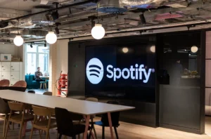 Sede do Spotify com telas digitais mostrando interface do app e crescimento global de usuários