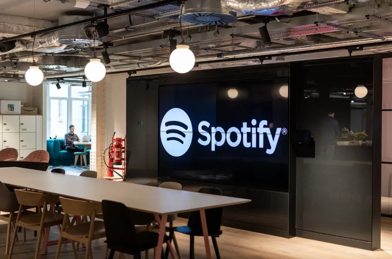 Sede do Spotify com telas digitais mostrando interface do app e crescimento global de usuários