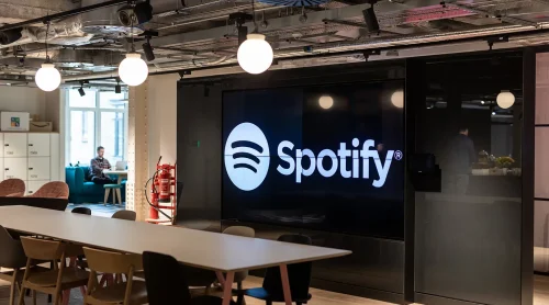 Sede do Spotify com telas digitais mostrando interface do app e crescimento global de usuários
